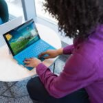 Person typing on a laptop at a small round table in an office lounge