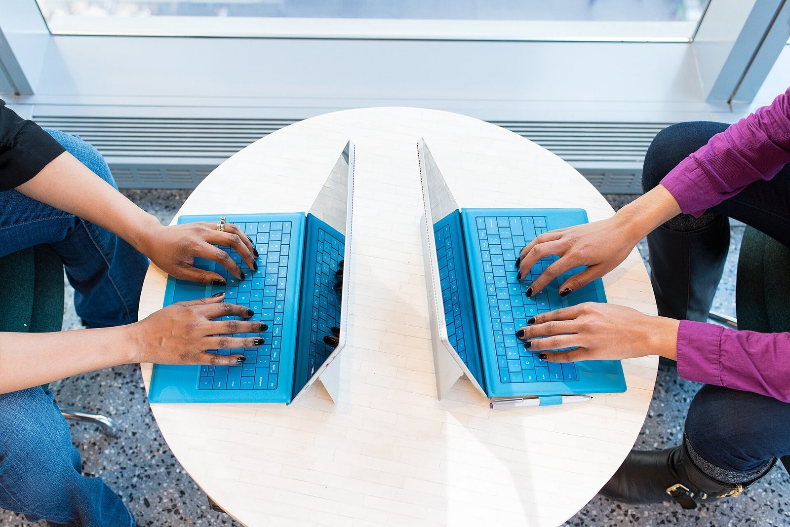Two people typing on laptops side by side at a shared table