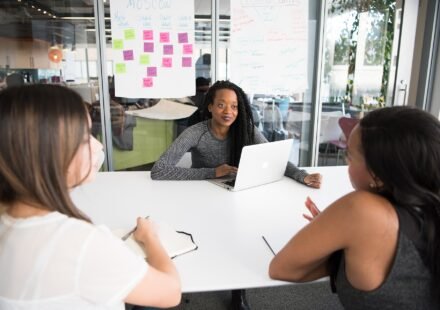 Three people collaborating around a laptop at a meeting table