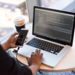 Developer working on a laptop with code on screen while holding a phone