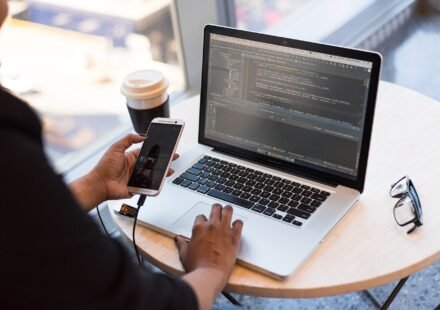 Developer working on a laptop with code on screen while holding a phone
