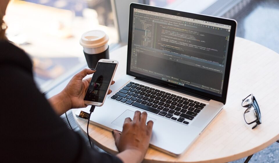 Jira Slack Integration 2026: Setup, @Jira Tickets and Channels Without the Noise Developer working on a laptop with code on screen while holding a phone