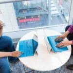Two colleagues working on laptops across a shared round table
