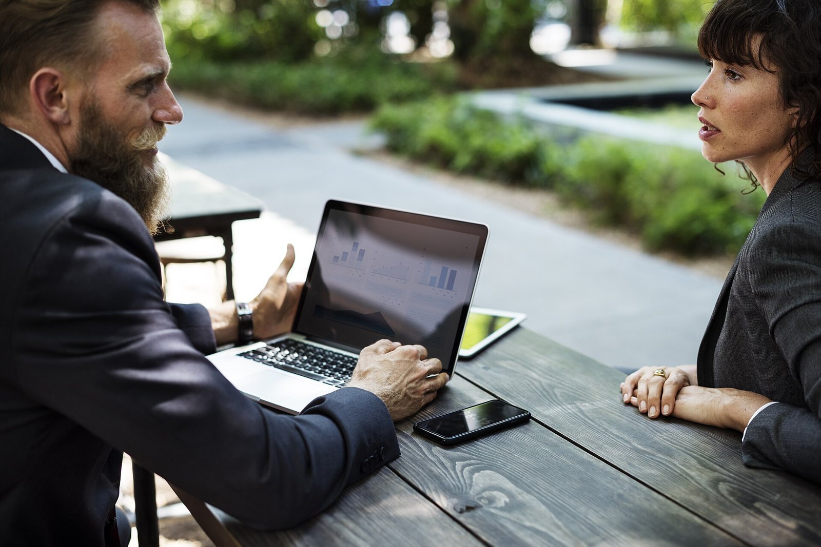 Two colleagues discussing work at an outdoor table with a laptop