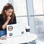 Woman sitting at a laptop with her hand on her chin, thinking through a problem