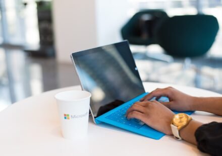 Laptop open on a desk next to a Microsoft coffee cup