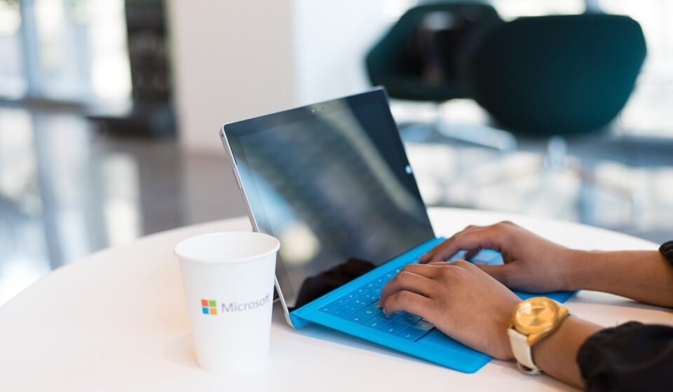 Laptop open on a desk next to a Microsoft coffee cup