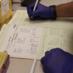 Researcher writing in a lab notebook beside sample tubes