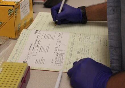 Researcher writing in a lab notebook beside sample tubes