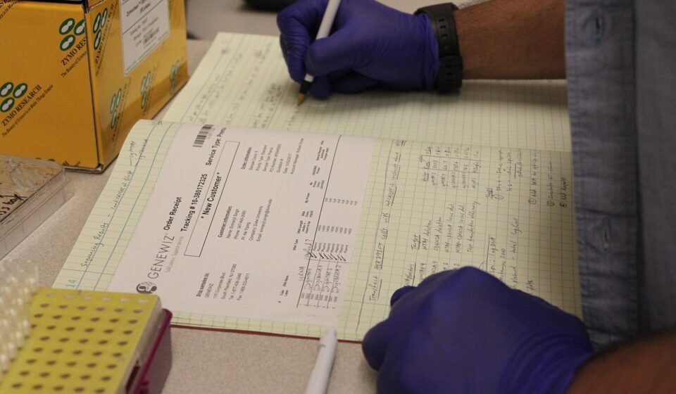 Notion vs Airtable for Academic Research (2026): Which One Fits Your Lab or Thesis? Researcher writing in a lab notebook beside sample tubes